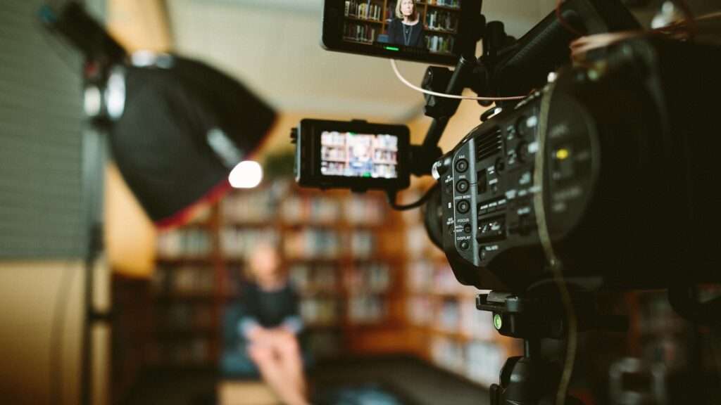 Seitliche Perspektive auf eine Kamera, die ein Interview mit einer Frau in einer Bibliothek filmt